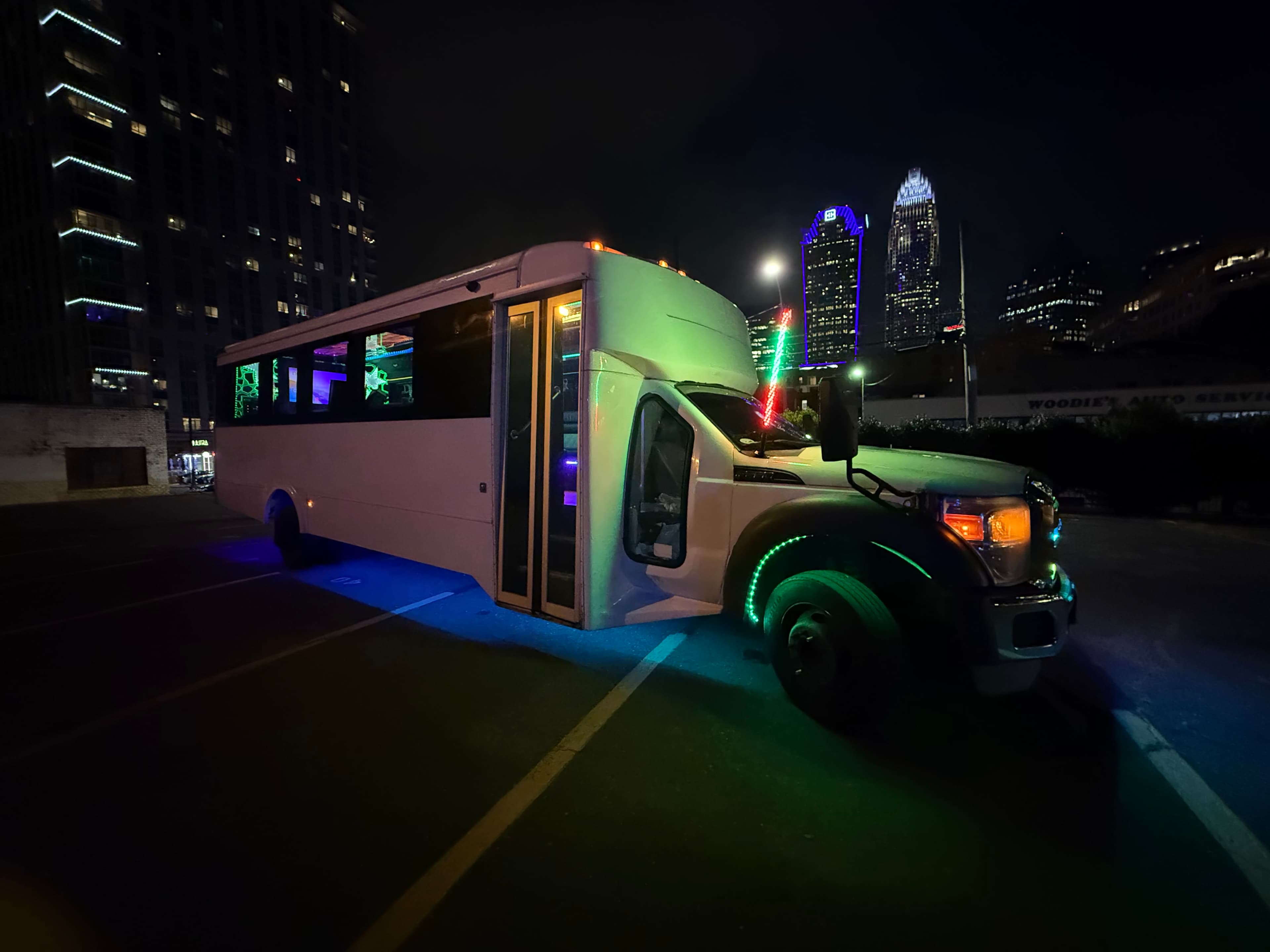 Concert transportation service in Charlotte with LED-lit party bus near the city skyline at night